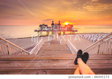Young man sitting on wooden pier enjoying sunrise 66445173