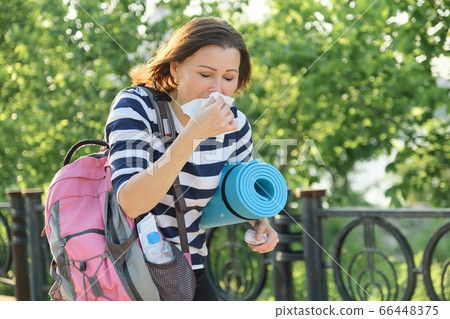Woman walking in the park with handkerchief, coughing and sneezing 66448375