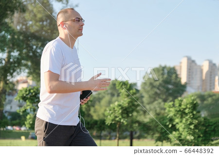 Middle aged male with glasses runs through city park with headphones 66448392