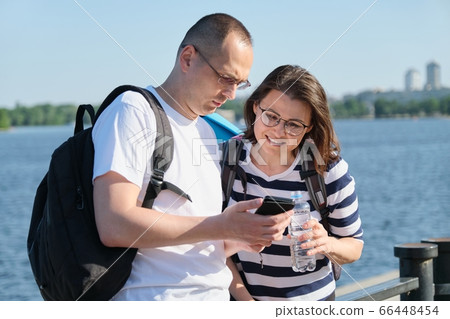 Outdoor mature couple using smartphone, man and woman talking walking in the park Outdoor mature couple using smartphone, man and woman talking walking in the park 66448454
