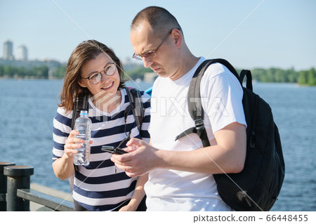Outdoor mature couple using smartphone, man and woman talking walking in the park Outdoor mature couple using smartphone, man and woman talking walking in the park 66448455