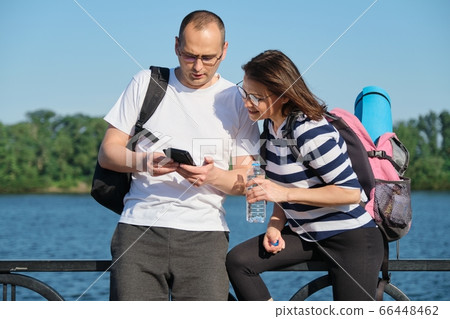Outdoor mature couple using smartphone, man and woman talking walking in the park Outdoor mature couple using smartphone, man and woman talking walking in the park 66448462