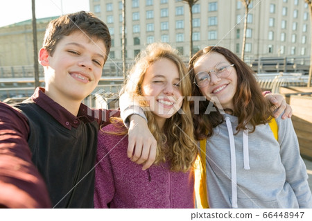 Portrait of three teen friends boy and two girls smiling and taking a selfie outdoors. Portrait of three teen friends boy and two girls smiling and taking a selfie outdoors. 66448947