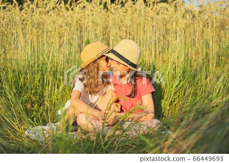 Two smiling girls sitting in grass, children talking 66449693