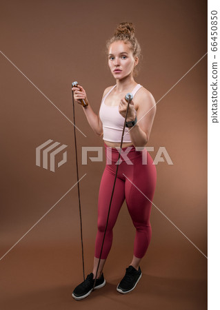 Pretty young fit sportswoman in activewear keeping right foot on skipping-rope Pretty young fit sportswoman in activewear keeping right foot on skipping-rope 66450850