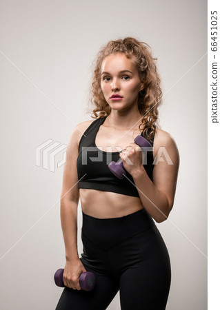 Pretty girl with blond curly hair holding dumbbells in hands during exercise Pretty girl with blond curly hair holding dumbbells in hands during exercise 66451025