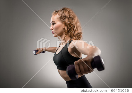Side view of young sportswoman in tracksuit lifting dumbbells and breathing Side view of young sportswoman in tracksuit lifting dumbbells and breathing 66451036