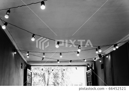 The ceiling in the street cafe is decorated with a garland with light bulbs. Monochrome black and 66452521