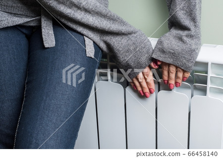 Closeup of warming frozen woman near radiator 66458140