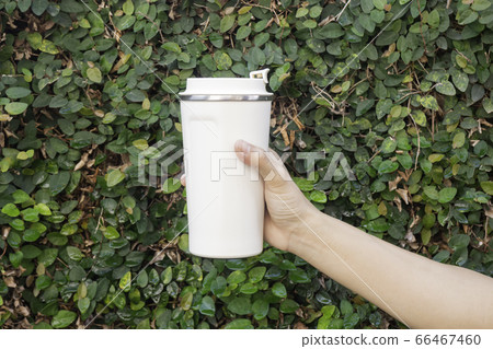 Aluminum thermos mug on hand with green leaves Aluminum thermos mug on hand with green leaves 66467460