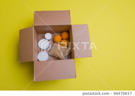 the main products for self-isolation in a box: cereals, buckwheat, fruit, canned food on a yellow background. home delivery. Assistance to population 66470657