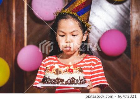 Cute asian child girl is blowing candles on delicious birthday cake in the party 66472321