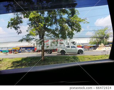 從車窗望去，中間地帶樹後對面車道上的白色卡車和商店招牌上寫著外語的風景 66472814