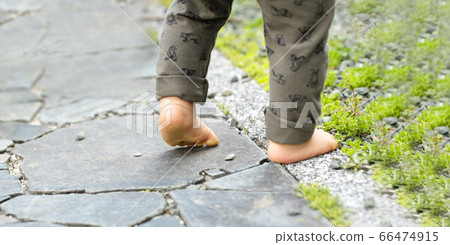 Both feet of a child walking barefoot on a cobblestone 66474915