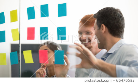 Smiling diverse employees working on project, looking on sticky papers Smiling diverse employees working on project, looking on sticky papers 66476582
