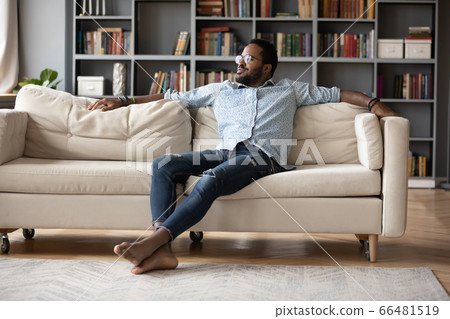 Carefree african man resting on sofa in cozy living room 66481519