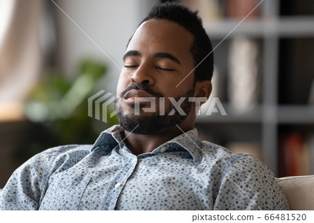 Close up African young man sit on couch closed eyes resting reduces fatigue 66481520