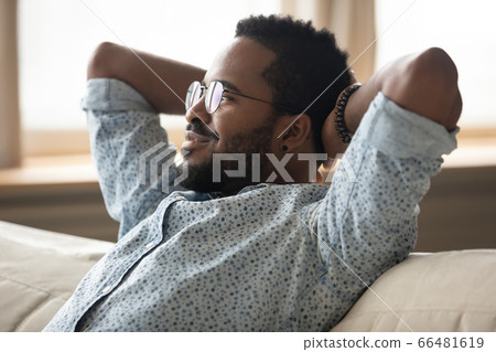 Calm African guy puts hands behind head relaxing on couch 66481619