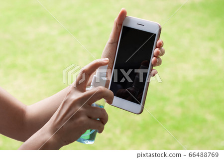 Thai woman wipes her hands with an alcohol based mobile smartphone washing spray. Coronavirus prevention for hand hygiene corona virus protection. COVID-19 prevention sanitizing inside. 66488769