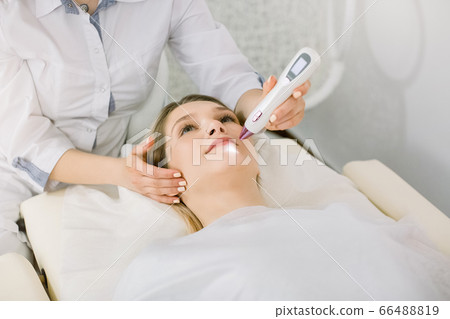 Cropped image of female surgeon beautician removing pigmentation and vascular nets on the skin of the patient, beautiful young woman, using laser tool. Laser cosmetology Cropped image of female surgeon beautician removing pigmentation and vascular nets on the skin of the patient, beautiful young woman, using laser tool. Laser cosmetology 66488819