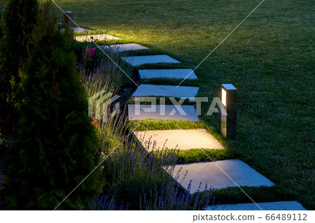marble path of square tiles illuminated by a lantern glowing with a warm light in a backyard garden with a flower bed and a lawn copy space. marble path of square tiles illuminated by a lantern glowing with a warm light in a backyard garden with a flower bed and a lawn copy space. 66489112
