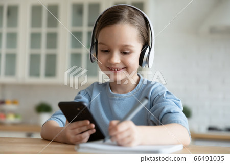 Little schoolgirl wears headphones use smartphone watching educational video 66491035