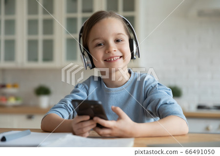 Schoolgirl study at home using wireless headphones and smartphone application Schoolgirl study at home using wireless headphones and smartphone application 66491050