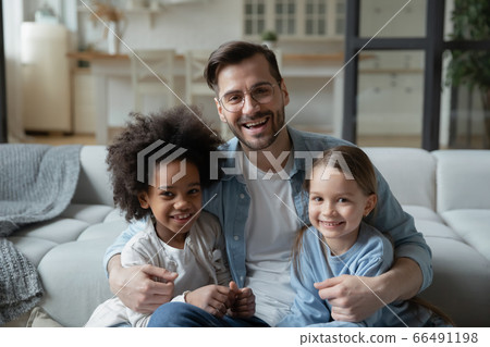 Father sit on sofa hugs caucasian and african little daughters 66491198