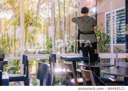 Back view of maid closes the glass window to turn on the air conditioner in the coffee shop. Back view of maid closes the glass window to turn on the air conditioner in the coffee shop. 66498521