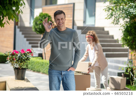 Smiling man holding a key from the new house and feeling great, his wife standing near the cardboards Smiling man holding a key from the new house and feeling great, his wife standing near the cardboards 66503218