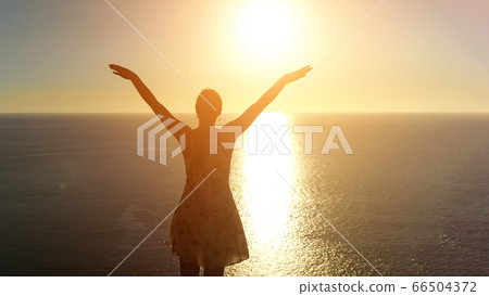 woman in summer dress raises hands on beach at sunset woman in summer dress raises hands on beach at sunset 66504372