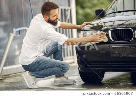 Man in a white shirt wipes a car in a car wash 66505907