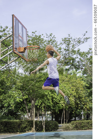 Basketball in hand man jumping Throw a basketball hoop Background tree in park. Basketball in hand man jumping Throw a basketball hoop Background tree in park. 66509087
