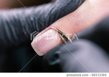 Close-up professional beautician hands working with electric drill on client fingernails. Procedure applying artificial fingernails. Hands of manicurist with tool. Manicurist in gloves removes cuticle Close-up professional beautician hands working with electric drill on client fingernails. Procedure applying artificial fingernails. Hands of manicurist with tool. Manicurist in gloves removes cuticle 66513369