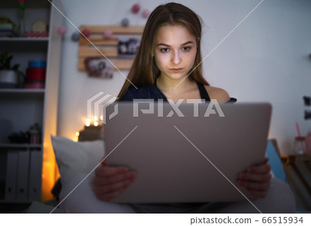 Sad and worried young girl with laptop sitting indoors, internet abuse concept. Sad and worried young girl with laptop sitting indoors, internet abuse concept. 66515934