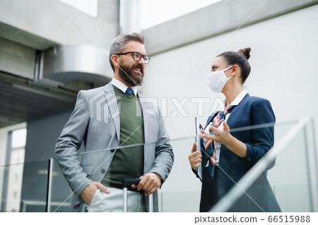 Flight attendant talking to businessman on airport, wearing face masks. 66515988