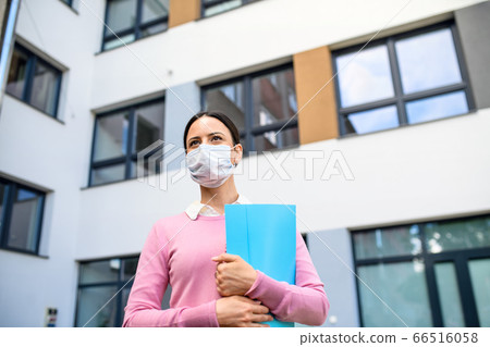 Low angle view of teacher with face mask after lockdown, walking in front of school. 66516058