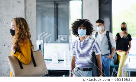 Young people with face masks back at work in office after lockdown, walking. 66516623
