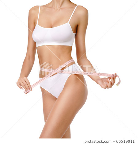 Slim tanned woman's body over gray background - waist measurement 66519011