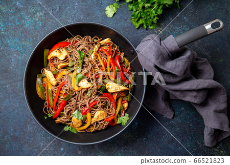 Japanese dish buckwheat soba noodles with chicken and vegetables carrot, bell pepper and green beans in wok on dark blue background Japanese dish buckwheat soba noodles with chicken and vegetables carrot, bell pepper and green beans in wok on dark blue background 66521823