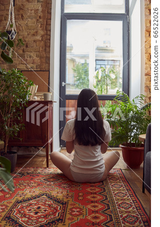 Pretty female sitting on a carpet looking at the window 66522026