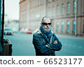 a man walks in the street, he has denim jacket, glasses, mustache and beard 66523177