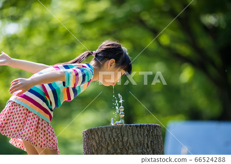 Cute kid drinking faucet water in midsummer park 66524288