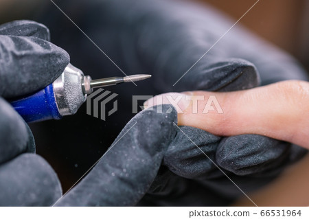 Manicurist use electric nail file drill in beauty salon. Perfect nails manicure process close up with burst flying debris. 66531964