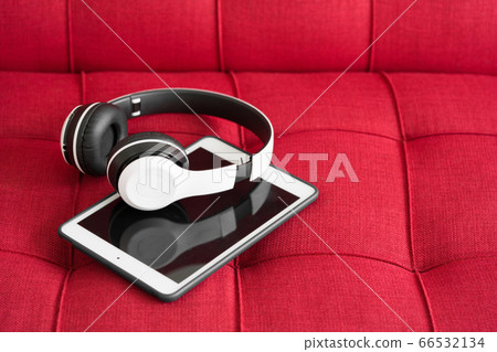 White modern headphones and tablet computer on red sofa 66532134