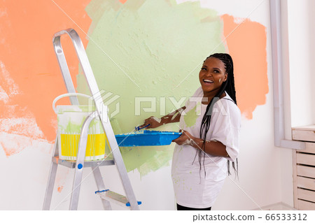 Young beautiful African American woman painting wall in her new apartment. Renovation and redecoration concept. Young beautiful African American woman painting wall in her new apartment. Renovation and redecoration concept. 66533312