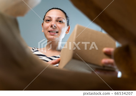 Caucasian woman opens craft paper delivery package with happy emotion. Caucasian woman opens craft paper delivery package with happy emotion. 66534207
