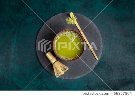 Wooden cup with green matcha tea, bamboo whisk and spoon on round shale serving board in center of emerald backdrop. Matcha tea - healthy detox superfood. View from above. Copy space for text. Wooden cup with green matcha tea, bamboo whisk and spoon on round shale serving board in center of emerald backdrop. Matcha tea - healthy detox superfood. View from above. Copy space for text. 66537864