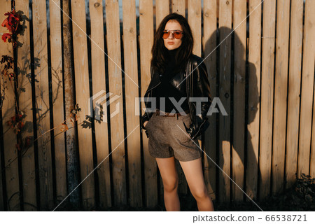 stylish young Caucasian girl brunette in a leather jacket and shorts in fashionable sunglasses stylish young Caucasian girl brunette in a leather jacket and shorts in fashionable sunglasses 66538721