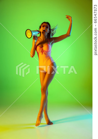 Beautiful girl in fashionable swimsuit isolated on gradient studio background in neon light. Summer, resort, fashion and weekend concept Beautiful girl in fashionable swimsuit isolated on gradient studio background in neon light. Summer, resort, fashion and weekend concept 66547873